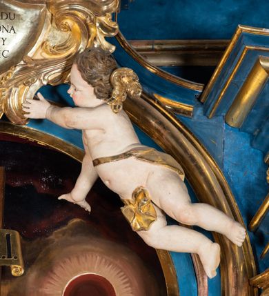 Zdjęcie nr 22: Ołtarz architektoniczny, jednoosiowy, jednokondygnacyjny ze zwieńczeniem. Na zdwojonych cokołach usytuowanych ukośnie względem osi po trzy kompozytowe kolumny opinające filary o gładkich trzonach podtrzymujących wyłamujące się nad nimi belkowanie z ćwierćkolistymi naczółkami. Na nich siedzące anioły z narzędzami męki Pańskiej. Pośrodku wnęka zamknięta półkoliście i wchodząca w partię belkowania z figurą Ukrzyżowanego. Nad wnęką dwa nagie putta trzymają kartusz z napisem: "DZIEŁO / NIE MAJĄC PRZYKŁADU / ŁASKA NIE ZASŁUŻONA / DAR NIE OCENIONY / MIŁOŚĆ BEZ GRANIC".  Zwieńczenie ujęte spływami wolutowymi, mocno zwężające się ku górze, zakończone gzymsem w formie łuku nadwieszonego. W polu owalny prześwit z glorią promienistą w chmurach z figurą Boga Ojca, puttami siedzącymi na gzymsie i główkami aniołów wśród chmur. Po bokach ołtarza dwie bramki z cokołami ujętymi spływami wolutowymi, na których figury św. Jana Chrzciciela i św. Jana Ewangelisty. Dekoracja ornamentalna w postaci rozłożystych liści na cokołach oraz liściastych, ażurowych uszy ujmujących nastawę. 