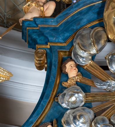 Zdjęcie nr 20: Ołtarz architektoniczny, jednoosiowy, jednokondygnacyjny ze zwieńczeniem. Na zdwojonych cokołach usytuowanych ukośnie względem osi po trzy kompozytowe kolumny opinające filary o gładkich trzonach podtrzymujących wyłamujące się nad nimi belkowanie z ćwierćkolistymi naczółkami. Na nich siedzące anioły z narzędzami męki Pańskiej. Pośrodku wnęka zamknięta półkoliście i wchodząca w partię belkowania z figurą Ukrzyżowanego. Nad wnęką dwa nagie putta trzymają kartusz z napisem: "DZIEŁO / NIE MAJĄC PRZYKŁADU / ŁASKA NIE ZASŁUŻONA / DAR NIE OCENIONY / MIŁOŚĆ BEZ GRANIC".  Zwieńczenie ujęte spływami wolutowymi, mocno zwężające się ku górze, zakończone gzymsem w formie łuku nadwieszonego. W polu owalny prześwit z glorią promienistą w chmurach z figurą Boga Ojca, puttami siedzącymi na gzymsie i główkami aniołów wśród chmur. Po bokach ołtarza dwie bramki z cokołami ujętymi spływami wolutowymi, na których figury św. Jana Chrzciciela i św. Jana Ewangelisty. Dekoracja ornamentalna w postaci rozłożystych liści na cokołach oraz liściastych, ażurowych uszy ujmujących nastawę. 