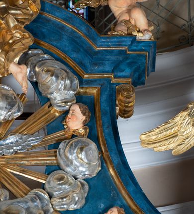 Zdjęcie nr 21: Ołtarz architektoniczny, jednoosiowy, jednokondygnacyjny ze zwieńczeniem. Na zdwojonych cokołach usytuowanych ukośnie względem osi po trzy kompozytowe kolumny opinające filary o gładkich trzonach podtrzymujących wyłamujące się nad nimi belkowanie z ćwierćkolistymi naczółkami. Na nich siedzące anioły z narzędzami męki Pańskiej. Pośrodku wnęka zamknięta półkoliście i wchodząca w partię belkowania z figurą Ukrzyżowanego. Nad wnęką dwa nagie putta trzymają kartusz z napisem: "DZIEŁO / NIE MAJĄC PRZYKŁADU / ŁASKA NIE ZASŁUŻONA / DAR NIE OCENIONY / MIŁOŚĆ BEZ GRANIC".  Zwieńczenie ujęte spływami wolutowymi, mocno zwężające się ku górze, zakończone gzymsem w formie łuku nadwieszonego. W polu owalny prześwit z glorią promienistą w chmurach z figurą Boga Ojca, puttami siedzącymi na gzymsie i główkami aniołów wśród chmur. Po bokach ołtarza dwie bramki z cokołami ujętymi spływami wolutowymi, na których figury św. Jana Chrzciciela i św. Jana Ewangelisty. Dekoracja ornamentalna w postaci rozłożystych liści na cokołach oraz liściastych, ażurowych uszy ujmujących nastawę. 