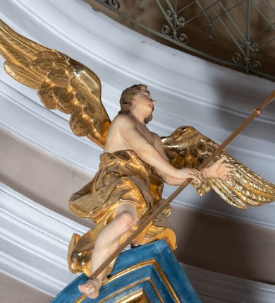 Zdjęcie nr 26: Ołtarz architektoniczny, jednoosiowy, jednokondygnacyjny ze zwieńczeniem. Na zdwojonych cokołach usytuowanych ukośnie względem osi po trzy kompozytowe kolumny opinające filary o gładkich trzonach podtrzymujących wyłamujące się nad nimi belkowanie z ćwierćkolistymi naczółkami. Na nich siedzące anioły z narzędzami męki Pańskiej. Pośrodku wnęka zamknięta półkoliście i wchodząca w partię belkowania z figurą Ukrzyżowanego. Nad wnęką dwa nagie putta trzymają kartusz z napisem: "DZIEŁO / NIE MAJĄC PRZYKŁADU / ŁASKA NIE ZASŁUŻONA / DAR NIE OCENIONY / MIŁOŚĆ BEZ GRANIC".  Zwieńczenie ujęte spływami wolutowymi, mocno zwężające się ku górze, zakończone gzymsem w formie łuku nadwieszonego. W polu owalny prześwit z glorią promienistą w chmurach z figurą Boga Ojca, puttami siedzącymi na gzymsie i główkami aniołów wśród chmur. Po bokach ołtarza dwie bramki z cokołami ujętymi spływami wolutowymi, na których figury św. Jana Chrzciciela i św. Jana Ewangelisty. Dekoracja ornamentalna w postaci rozłożystych liści na cokołach oraz liściastych, ażurowych uszy ujmujących nastawę. 