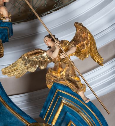 Zdjęcie nr 37: Ołtarz architektoniczny, jednoosiowy, jednokondygnacyjny ze zwieńczeniem. Na zdwojonych cokołach usytuowanych ukośnie względem osi po trzy kompozytowe kolumny opinające filary o gładkich trzonach podtrzymujących wyłamujące się nad nimi belkowanie z ćwierćkolistymi naczółkami. Na nich siedzące anioły z narzędzami męki Pańskiej. Pośrodku wnęka zamknięta półkoliście i wchodząca w partię belkowania z figurą Ukrzyżowanego. Nad wnęką dwa nagie putta trzymają kartusz z napisem: &quot;DZIEŁO / NIE MAJĄC PRZYKŁADU / ŁASKA NIE ZASŁUŻONA / DAR NIE OCENIONY / MIŁOŚĆ BEZ GRANIC&quot;.  Zwieńczenie ujęte spływami wolutowymi, mocno zwężające się ku górze, zakończone gzymsem w formie łuku nadwieszonego. W polu owalny prześwit z glorią promienistą w chmurach z figurą Boga Ojca, puttami siedzącymi na gzymsie i główkami aniołów wśród chmur. Po bokach ołtarza dwie bramki z cokołami ujętymi spływami wolutowymi, na których figury św. Jana Chrzciciela i św. Jana Ewangelisty. Dekoracja ornamentalna w postaci rozłożystych liści na cokołach oraz liściastych, ażurowych uszy ujmujących nastawę. 