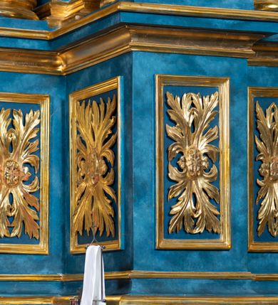 Zdjęcie nr 76: Ołtarz architektoniczny, jednoosiowy, jednokondygnacyjny ze zwieńczeniem. Na zdwojonych cokołach usytuowanych ukośnie względem osi po trzy kompozytowe kolumny opinające filary o gładkich trzonach podtrzymujących wyłamujące się nad nimi belkowanie z ćwierćkolistymi naczółkami. Na nich siedzące anioły z narzędzami męki Pańskiej. Pośrodku wnęka zamknięta półkoliście i wchodząca w partię belkowania z figurą Ukrzyżowanego. Nad wnęką dwa nagie putta trzymają kartusz z napisem: "DZIEŁO / NIE MAJĄC PRZYKŁADU / ŁASKA NIE ZASŁUŻONA / DAR NIE OCENIONY / MIŁOŚĆ BEZ GRANIC".  Zwieńczenie ujęte spływami wolutowymi, mocno zwężające się ku górze, zakończone gzymsem w formie łuku nadwieszonego. W polu owalny prześwit z glorią promienistą w chmurach z figurą Boga Ojca, puttami siedzącymi na gzymsie i główkami aniołów wśród chmur. Po bokach ołtarza dwie bramki z cokołami ujętymi spływami wolutowymi, na których figury św. Jana Chrzciciela i św. Jana Ewangelisty. Dekoracja ornamentalna w postaci rozłożystych liści na cokołach oraz liściastych, ażurowych uszy ujmujących nastawę. 