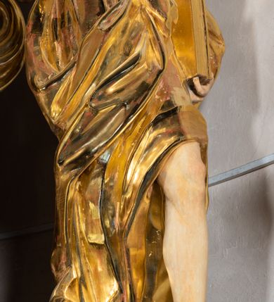 Zdjęcie nr 56: Ołtarz architektoniczny, jednoosiowy, jednokondygnacyjny ze zwieńczeniem. Na zdwojonych cokołach usytuowanych ukośnie względem osi po trzy kompozytowe kolumny opinające filary o gładkich trzonach podtrzymujących wyłamujące się nad nimi belkowanie z ćwierćkolistymi naczółkami. Na nich siedzące anioły z narzędzami męki Pańskiej. Pośrodku wnęka zamknięta półkoliście i wchodząca w partię belkowania z figurą Ukrzyżowanego. Nad wnęką dwa nagie putta trzymają kartusz z napisem: &quot;DZIEŁO / NIE MAJĄC PRZYKŁADU / ŁASKA NIE ZASŁUŻONA / DAR NIE OCENIONY / MIŁOŚĆ BEZ GRANIC&quot;.  Zwieńczenie ujęte spływami wolutowymi, mocno zwężające się ku górze, zakończone gzymsem w formie łuku nadwieszonego. W polu owalny prześwit z glorią promienistą w chmurach z figurą Boga Ojca, puttami siedzącymi na gzymsie i główkami aniołów wśród chmur. Po bokach ołtarza dwie bramki z cokołami ujętymi spływami wolutowymi, na których figury św. Jana Chrzciciela i św. Jana Ewangelisty. Dekoracja ornamentalna w postaci rozłożystych liści na cokołach oraz liściastych, ażurowych uszy ujmujących nastawę. 