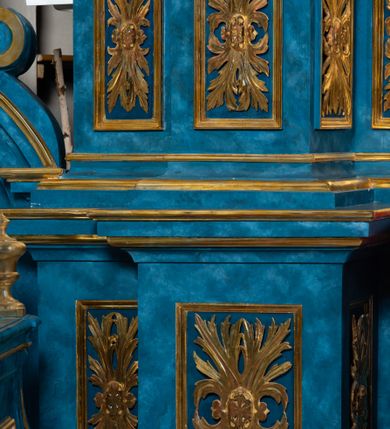 Zdjęcie nr 79: Ołtarz architektoniczny, jednoosiowy, jednokondygnacyjny ze zwieńczeniem. Na zdwojonych cokołach usytuowanych ukośnie względem osi po trzy kompozytowe kolumny opinające filary o gładkich trzonach podtrzymujących wyłamujące się nad nimi belkowanie z ćwierćkolistymi naczółkami. Na nich siedzące anioły z narzędzami męki Pańskiej. Pośrodku wnęka zamknięta półkoliście i wchodząca w partię belkowania z figurą Ukrzyżowanego. Nad wnęką dwa nagie putta trzymają kartusz z napisem: &quot;DZIEŁO / NIE MAJĄC PRZYKŁADU / ŁASKA NIE ZASŁUŻONA / DAR NIE OCENIONY / MIŁOŚĆ BEZ GRANIC&quot;.  Zwieńczenie ujęte spływami wolutowymi, mocno zwężające się ku górze, zakończone gzymsem w formie łuku nadwieszonego. W polu owalny prześwit z glorią promienistą w chmurach z figurą Boga Ojca, puttami siedzącymi na gzymsie i główkami aniołów wśród chmur. Po bokach ołtarza dwie bramki z cokołami ujętymi spływami wolutowymi, na których figury św. Jana Chrzciciela i św. Jana Ewangelisty. Dekoracja ornamentalna w postaci rozłożystych liści na cokołach oraz liściastych, ażurowych uszy ujmujących nastawę. 