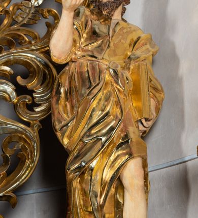 Zdjęcie nr 65: Ołtarz architektoniczny, jednoosiowy, jednokondygnacyjny ze zwieńczeniem. Na zdwojonych cokołach usytuowanych ukośnie względem osi po trzy kompozytowe kolumny opinające filary o gładkich trzonach podtrzymujących wyłamujące się nad nimi belkowanie z ćwierćkolistymi naczółkami. Na nich siedzące anioły z narzędzami męki Pańskiej. Pośrodku wnęka zamknięta półkoliście i wchodząca w partię belkowania z figurą Ukrzyżowanego. Nad wnęką dwa nagie putta trzymają kartusz z napisem: &quot;DZIEŁO / NIE MAJĄC PRZYKŁADU / ŁASKA NIE ZASŁUŻONA / DAR NIE OCENIONY / MIŁOŚĆ BEZ GRANIC&quot;.  Zwieńczenie ujęte spływami wolutowymi, mocno zwężające się ku górze, zakończone gzymsem w formie łuku nadwieszonego. W polu owalny prześwit z glorią promienistą w chmurach z figurą Boga Ojca, puttami siedzącymi na gzymsie i główkami aniołów wśród chmur. Po bokach ołtarza dwie bramki z cokołami ujętymi spływami wolutowymi, na których figury św. Jana Chrzciciela i św. Jana Ewangelisty. Dekoracja ornamentalna w postaci rozłożystych liści na cokołach oraz liściastych, ażurowych uszy ujmujących nastawę. 