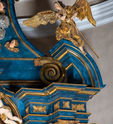 Zdjęcie nr 85: Ołtarz architektoniczny, jednoosiowy, jednokondygnacyjny ze zwieńczeniem. Na zdwojonych cokołach usytuowanych ukośnie względem osi po trzy kompozytowe kolumny opinające filary o gładkich trzonach podtrzymujących wyłamujące się nad nimi belkowanie z ćwierćkolistymi naczółkami. Na nich siedzące anioły z narzędzami męki Pańskiej. Pośrodku wnęka zamknięta półkoliście i wchodząca w partię belkowania z figurą Ukrzyżowanego. Nad wnęką dwa nagie putta trzymają kartusz z napisem: "DZIEŁO / NIE MAJĄC PRZYKŁADU / ŁASKA NIE ZASŁUŻONA / DAR NIE OCENIONY / MIŁOŚĆ BEZ GRANIC".  Zwieńczenie ujęte spływami wolutowymi, mocno zwężające się ku górze, zakończone gzymsem w formie łuku nadwieszonego. W polu owalny prześwit z glorią promienistą w chmurach z figurą Boga Ojca, puttami siedzącymi na gzymsie i główkami aniołów wśród chmur. Po bokach ołtarza dwie bramki z cokołami ujętymi spływami wolutowymi, na których figury św. Jana Chrzciciela i św. Jana Ewangelisty. Dekoracja ornamentalna w postaci rozłożystych liści na cokołach oraz liściastych, ażurowych uszy ujmujących nastawę. 