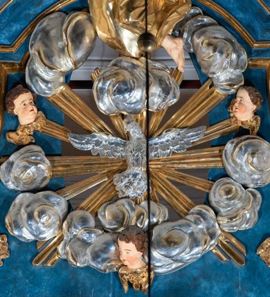 Zdjęcie nr 86: Ołtarz architektoniczny, jednoosiowy, jednokondygnacyjny ze zwieńczeniem. Na zdwojonych cokołach usytuowanych ukośnie względem osi po trzy kompozytowe kolumny opinające filary o gładkich trzonach podtrzymujących wyłamujące się nad nimi belkowanie z ćwierćkolistymi naczółkami. Na nich siedzące anioły z narzędzami męki Pańskiej. Pośrodku wnęka zamknięta półkoliście i wchodząca w partię belkowania z figurą Ukrzyżowanego. Nad wnęką dwa nagie putta trzymają kartusz z napisem: &quot;DZIEŁO / NIE MAJĄC PRZYKŁADU / ŁASKA NIE ZASŁUŻONA / DAR NIE OCENIONY / MIŁOŚĆ BEZ GRANIC&quot;.  Zwieńczenie ujęte spływami wolutowymi, mocno zwężające się ku górze, zakończone gzymsem w formie łuku nadwieszonego. W polu owalny prześwit z glorią promienistą w chmurach z figurą Boga Ojca, puttami siedzącymi na gzymsie i główkami aniołów wśród chmur. Po bokach ołtarza dwie bramki z cokołami ujętymi spływami wolutowymi, na których figury św. Jana Chrzciciela i św. Jana Ewangelisty. Dekoracja ornamentalna w postaci rozłożystych liści na cokołach oraz liściastych, ażurowych uszy ujmujących nastawę. 