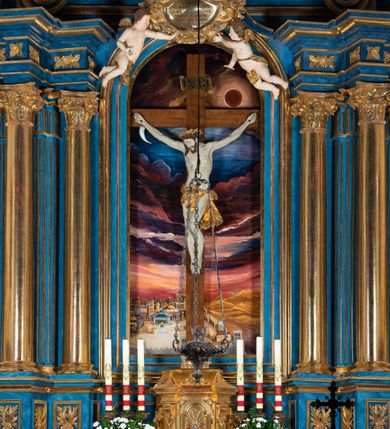 Zdjęcie nr 89: Ołtarz architektoniczny, jednoosiowy, jednokondygnacyjny ze zwieńczeniem. Na zdwojonych cokołach usytuowanych ukośnie względem osi po trzy kompozytowe kolumny opinające filary o gładkich trzonach podtrzymujących wyłamujące się nad nimi belkowanie z ćwierćkolistymi naczółkami. Na nich siedzące anioły z narzędzami męki Pańskiej. Pośrodku wnęka zamknięta półkoliście i wchodząca w partię belkowania z figurą Ukrzyżowanego. Nad wnęką dwa nagie putta trzymają kartusz z napisem: &quot;DZIEŁO / NIE MAJĄC PRZYKŁADU / ŁASKA NIE ZASŁUŻONA / DAR NIE OCENIONY / MIŁOŚĆ BEZ GRANIC&quot;.  Zwieńczenie ujęte spływami wolutowymi, mocno zwężające się ku górze, zakończone gzymsem w formie łuku nadwieszonego. W polu owalny prześwit z glorią promienistą w chmurach z figurą Boga Ojca, puttami siedzącymi na gzymsie i główkami aniołów wśród chmur. Po bokach ołtarza dwie bramki z cokołami ujętymi spływami wolutowymi, na których figury św. Jana Chrzciciela i św. Jana Ewangelisty. Dekoracja ornamentalna w postaci rozłożystych liści na cokołach oraz liściastych, ażurowych uszy ujmujących nastawę. 