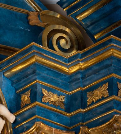 Zdjęcie nr 93: Ołtarz architektoniczny, jednoosiowy, jednokondygnacyjny ze zwieńczeniem. Na zdwojonych cokołach usytuowanych ukośnie względem osi po trzy kompozytowe kolumny opinające filary o gładkich trzonach podtrzymujących wyłamujące się nad nimi belkowanie z ćwierćkolistymi naczółkami. Na nich siedzące anioły z narzędzami męki Pańskiej. Pośrodku wnęka zamknięta półkoliście i wchodząca w partię belkowania z figurą Ukrzyżowanego. Nad wnęką dwa nagie putta trzymają kartusz z napisem: "DZIEŁO / NIE MAJĄC PRZYKŁADU / ŁASKA NIE ZASŁUŻONA / DAR NIE OCENIONY / MIŁOŚĆ BEZ GRANIC".  Zwieńczenie ujęte spływami wolutowymi, mocno zwężające się ku górze, zakończone gzymsem w formie łuku nadwieszonego. W polu owalny prześwit z glorią promienistą w chmurach z figurą Boga Ojca, puttami siedzącymi na gzymsie i główkami aniołów wśród chmur. Po bokach ołtarza dwie bramki z cokołami ujętymi spływami wolutowymi, na których figury św. Jana Chrzciciela i św. Jana Ewangelisty. Dekoracja ornamentalna w postaci rozłożystych liści na cokołach oraz liściastych, ażurowych uszy ujmujących nastawę. 