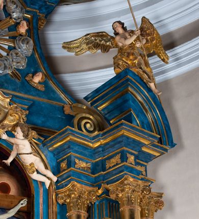 Zdjęcie nr 94: Ołtarz architektoniczny, jednoosiowy, jednokondygnacyjny ze zwieńczeniem. Na zdwojonych cokołach usytuowanych ukośnie względem osi po trzy kompozytowe kolumny opinające filary o gładkich trzonach podtrzymujących wyłamujące się nad nimi belkowanie z ćwierćkolistymi naczółkami. Na nich siedzące anioły z narzędzami męki Pańskiej. Pośrodku wnęka zamknięta półkoliście i wchodząca w partię belkowania z figurą Ukrzyżowanego. Nad wnęką dwa nagie putta trzymają kartusz z napisem: &quot;DZIEŁO / NIE MAJĄC PRZYKŁADU / ŁASKA NIE ZASŁUŻONA / DAR NIE OCENIONY / MIŁOŚĆ BEZ GRANIC&quot;.  Zwieńczenie ujęte spływami wolutowymi, mocno zwężające się ku górze, zakończone gzymsem w formie łuku nadwieszonego. W polu owalny prześwit z glorią promienistą w chmurach z figurą Boga Ojca, puttami siedzącymi na gzymsie i główkami aniołów wśród chmur. Po bokach ołtarza dwie bramki z cokołami ujętymi spływami wolutowymi, na których figury św. Jana Chrzciciela i św. Jana Ewangelisty. Dekoracja ornamentalna w postaci rozłożystych liści na cokołach oraz liściastych, ażurowych uszy ujmujących nastawę. 
