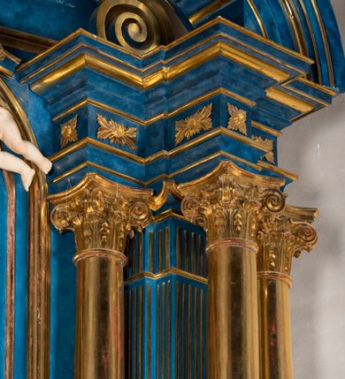 Zdjęcie nr 96: Ołtarz architektoniczny, jednoosiowy, jednokondygnacyjny ze zwieńczeniem. Na zdwojonych cokołach usytuowanych ukośnie względem osi po trzy kompozytowe kolumny opinające filary o gładkich trzonach podtrzymujących wyłamujące się nad nimi belkowanie z ćwierćkolistymi naczółkami. Na nich siedzące anioły z narzędzami męki Pańskiej. Pośrodku wnęka zamknięta półkoliście i wchodząca w partię belkowania z figurą Ukrzyżowanego. Nad wnęką dwa nagie putta trzymają kartusz z napisem: "DZIEŁO / NIE MAJĄC PRZYKŁADU / ŁASKA NIE ZASŁUŻONA / DAR NIE OCENIONY / MIŁOŚĆ BEZ GRANIC".  Zwieńczenie ujęte spływami wolutowymi, mocno zwężające się ku górze, zakończone gzymsem w formie łuku nadwieszonego. W polu owalny prześwit z glorią promienistą w chmurach z figurą Boga Ojca, puttami siedzącymi na gzymsie i główkami aniołów wśród chmur. Po bokach ołtarza dwie bramki z cokołami ujętymi spływami wolutowymi, na których figury św. Jana Chrzciciela i św. Jana Ewangelisty. Dekoracja ornamentalna w postaci rozłożystych liści na cokołach oraz liściastych, ażurowych uszy ujmujących nastawę. 