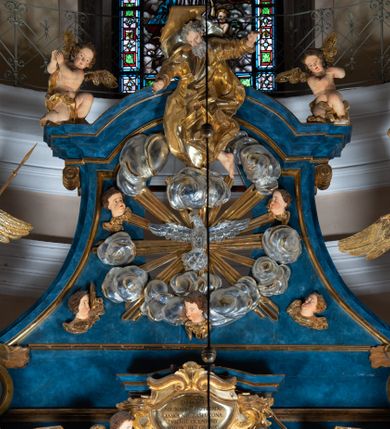 Zdjęcie nr 97: Ołtarz architektoniczny, jednoosiowy, jednokondygnacyjny ze zwieńczeniem. Na zdwojonych cokołach usytuowanych ukośnie względem osi po trzy kompozytowe kolumny opinające filary o gładkich trzonach podtrzymujących wyłamujące się nad nimi belkowanie z ćwierćkolistymi naczółkami. Na nich siedzące anioły z narzędzami męki Pańskiej. Pośrodku wnęka zamknięta półkoliście i wchodząca w partię belkowania z figurą Ukrzyżowanego. Nad wnęką dwa nagie putta trzymają kartusz z napisem: &quot;DZIEŁO / NIE MAJĄC PRZYKŁADU / ŁASKA NIE ZASŁUŻONA / DAR NIE OCENIONY / MIŁOŚĆ BEZ GRANIC&quot;.  Zwieńczenie ujęte spływami wolutowymi, mocno zwężające się ku górze, zakończone gzymsem w formie łuku nadwieszonego. W polu owalny prześwit z glorią promienistą w chmurach z figurą Boga Ojca, puttami siedzącymi na gzymsie i główkami aniołów wśród chmur. Po bokach ołtarza dwie bramki z cokołami ujętymi spływami wolutowymi, na których figury św. Jana Chrzciciela i św. Jana Ewangelisty. Dekoracja ornamentalna w postaci rozłożystych liści na cokołach oraz liściastych, ażurowych uszy ujmujących nastawę. 