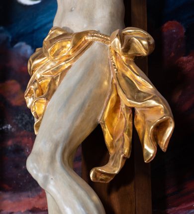 Zdjęcie nr 53: Ołtarz architektoniczny, jednoosiowy, jednokondygnacyjny ze zwieńczeniem. Na zdwojonych cokołach usytuowanych ukośnie względem osi po trzy kompozytowe kolumny opinające filary o gładkich trzonach podtrzymujących wyłamujące się nad nimi belkowanie z ćwierćkolistymi naczółkami. Na nich siedzące anioły z narzędzami męki Pańskiej. Pośrodku wnęka zamknięta półkoliście i wchodząca w partię belkowania z figurą Ukrzyżowanego. Nad wnęką dwa nagie putta trzymają kartusz z napisem: &quot;DZIEŁO / NIE MAJĄC PRZYKŁADU / ŁASKA NIE ZASŁUŻONA / DAR NIE OCENIONY / MIŁOŚĆ BEZ GRANIC&quot;.  Zwieńczenie ujęte spływami wolutowymi, mocno zwężające się ku górze, zakończone gzymsem w formie łuku nadwieszonego. W polu owalny prześwit z glorią promienistą w chmurach z figurą Boga Ojca, puttami siedzącymi na gzymsie i główkami aniołów wśród chmur. Po bokach ołtarza dwie bramki z cokołami ujętymi spływami wolutowymi, na których figury św. Jana Chrzciciela i św. Jana Ewangelisty. Dekoracja ornamentalna w postaci rozłożystych liści na cokołach oraz liściastych, ażurowych uszy ujmujących nastawę. 