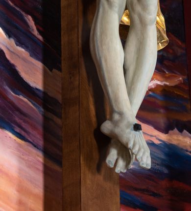 Zdjęcie nr 54: Ołtarz architektoniczny, jednoosiowy, jednokondygnacyjny ze zwieńczeniem. Na zdwojonych cokołach usytuowanych ukośnie względem osi po trzy kompozytowe kolumny opinające filary o gładkich trzonach podtrzymujących wyłamujące się nad nimi belkowanie z ćwierćkolistymi naczółkami. Na nich siedzące anioły z narzędzami męki Pańskiej. Pośrodku wnęka zamknięta półkoliście i wchodząca w partię belkowania z figurą Ukrzyżowanego. Nad wnęką dwa nagie putta trzymają kartusz z napisem: &quot;DZIEŁO / NIE MAJĄC PRZYKŁADU / ŁASKA NIE ZASŁUŻONA / DAR NIE OCENIONY / MIŁOŚĆ BEZ GRANIC&quot;.  Zwieńczenie ujęte spływami wolutowymi, mocno zwężające się ku górze, zakończone gzymsem w formie łuku nadwieszonego. W polu owalny prześwit z glorią promienistą w chmurach z figurą Boga Ojca, puttami siedzącymi na gzymsie i główkami aniołów wśród chmur. Po bokach ołtarza dwie bramki z cokołami ujętymi spływami wolutowymi, na których figury św. Jana Chrzciciela i św. Jana Ewangelisty. Dekoracja ornamentalna w postaci rozłożystych liści na cokołach oraz liściastych, ażurowych uszy ujmujących nastawę. 