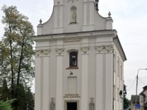 Zdjęcie nr 1:  Kościół usytuowany jest za północną pierzeją zabudowy rynku, w bezpośrednim sąsiedztwie świątyni parafialnej, po jej południowo-wschodniej stronie. 
Kościół orientowany, jest budowlą murowaną z cegły i kamienia (grubość murów od 70 do 160 cm), na rzucie podłużnym (24 m długość, 8,5 m szerokość). Korpus jednonawowy, trójprzęsłowy, prezbiterium jednoprzęsłowe, zamknięte półkolistą absydą, z dwukondygnacyjną przyległością od północy (zakrystia w przyziemiu). Nawę i prezbiterium przekrywa sklepienie kolebkowe z gurtami wspartymi na parach pilastrów dźwigających wydatne, obiegające wnętrze belkowanie. Nawę od prezbiterium oddziela półkolista arkada łuku tęczowego. Wnętrze doświetlają dwa rzędy okien zamkniętych łukami odcinkowymi. Artykulację ścian na zewnątrz stanowią płyciny ujmujące pary okien. Trójosiową fasadę artykułują pary osadzonych na cokole pilastrów – po dwie po bokach i jedna w polu środkowym wspierające belkowanie. W osi środkowej jest umiejscowiony ujęty profilowanym obramieniem otwór wejściowy z dwuskrzydłowymi drzwiami. Wyżej jest płytka, prostokątna wnęka, u góry zaś okno zamknięte łukiem odcinkowym. W osiach bocznych na cokole fasady osadzona para niszy z rzeźbami św. Piotra po lewej stronie i św. Pawła po prawej. Kapitele pilastrów zdobione motywami festonów owocowo-kwiatowych.   
Szczyt fasady ujęty parą spływów, zamknięty trójkątnie, po bokach flankowany parą cokołów zwieńczonych wazonami, pole środkowe wydzielone dwiema parami pilastrów zawiera półkoliście zamkniętą niszę z figurą Matki Boskiej, wyżej trójkąt Opatrzności Bożej ujęty promienistą glorią. Dachy korpusu i prezbiterium dwuspadowe, nad pierwszym przęsłem wieżyczka na sygnaturkę w formie latarni. Dach nad przyległością pulpitowy. Tynki kościoła w odcieniach bieli i szarości. 
