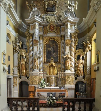 Zdjęcie nr 4:  Kościół usytuowany jest za północną pierzeją zabudowy rynku, w bezpośrednim sąsiedztwie świątyni parafialnej, po jej południowo-wschodniej stronie. 
Kościół orientowany, jest budowlą murowaną z cegły i kamienia (grubość murów od 70 do 160 cm), na rzucie podłużnym (24 m długość, 8,5 m szerokość). Korpus jednonawowy, trójprzęsłowy, prezbiterium jednoprzęsłowe, zamknięte półkolistą absydą, z dwukondygnacyjną przyległością od północy (zakrystia w przyziemiu). Nawę i prezbiterium przekrywa sklepienie kolebkowe z gurtami wspartymi na parach pilastrów dźwigających wydatne, obiegające wnętrze belkowanie. Nawę od prezbiterium oddziela półkolista arkada łuku tęczowego. Wnętrze doświetlają dwa rzędy okien zamkniętych łukami odcinkowymi. Artykulację ścian na zewnątrz stanowią płyciny ujmujące pary okien. Trójosiową fasadę artykułują pary osadzonych na cokole pilastrów – po dwie po bokach i jedna w polu środkowym wspierające belkowanie. W osi środkowej jest umiejscowiony ujęty profilowanym obramieniem otwór wejściowy z dwuskrzydłowymi drzwiami. Wyżej jest płytka, prostokątna wnęka, u góry zaś okno zamknięte łukiem odcinkowym. W osiach bocznych na cokole fasady osadzona para niszy z rzeźbami św. Piotra po lewej stronie i św. Pawła po prawej. Kapitele pilastrów zdobione motywami festonów owocowo-kwiatowych.   
Szczyt fasady ujęty parą spływów, zamknięty trójkątnie, po bokach flankowany parą cokołów zwieńczonych wazonami, pole środkowe wydzielone dwiema parami pilastrów zawiera półkoliście zamkniętą niszę z figurą Matki Boskiej, wyżej trójkąt Opatrzności Bożej ujęty promienistą glorią. Dachy korpusu i prezbiterium dwuspadowe, nad pierwszym przęsłem wieżyczka na sygnaturkę w formie latarni. Dach nad przyległością pulpitowy. Tynki kościoła w odcieniach bieli i szarości. 
