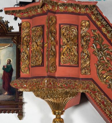 Zdjęcie nr 3: Ambona przyścienna dostępna jednotraktraktowymi schodami z pełną balustradą od strony wschodniej. Kosz na rzucie owalnym, opięty dostawionymi do boków pilastrami na rzucie trójkąta. W dolnej części złocony z podwieszoną szyszką. Podstawa walcowato wypukła dekorowana suchym akantem i jajownikiem. W polach kosza płyciny w kształcie stojącego prostokąta z symetryczną, złoconą dekoracją akantową. Trzony pilastrów wypełnione złoconym akantem o esowatym przebiegu wici. W zwieńczeniu wypukły, profilowany gzyms dekorowany palmetami I jajownikiem. Balustrada schodów zakończona pilastrem z prostokątną płyciną. W polu złocona dekoracją z suchego akantu. Struktura malowana w odcieniach ciemnej czerwieni i brązu, ornamentyka złocona.