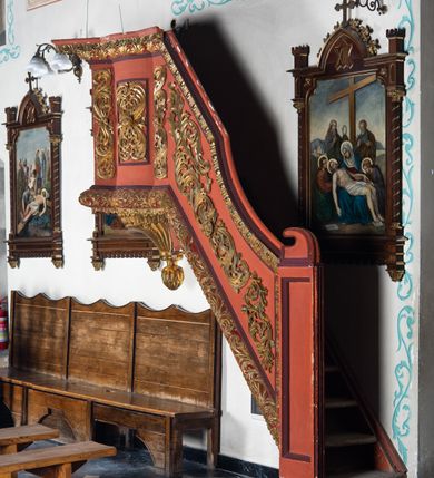 Zdjęcie nr 2: Ambona przyścienna dostępna jednotraktraktowymi schodami z pełną balustradą od strony wschodniej. Kosz na rzucie owalnym, opięty dostawionymi do boków pilastrami na rzucie trójkąta. W dolnej części złocony z podwieszoną szyszką. Podstawa walcowato wypukła dekorowana suchym akantem i jajownikiem. W polach kosza płyciny w kształcie stojącego prostokąta z symetryczną, złoconą dekoracją akantową. Trzony pilastrów wypełnione złoconym akantem o esowatym przebiegu wici. W zwieńczeniu wypukły, profilowany gzyms dekorowany palmetami I jajownikiem. Balustrada schodów zakończona pilastrem z prostokątną płyciną. W polu złocona dekoracją z suchego akantu. Struktura malowana w odcieniach ciemnej czerwieni i brązu, ornamentyka złocona.