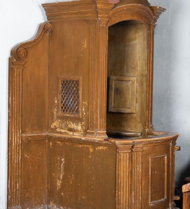 Zdjęcie nr 1: Konfesjonał ustawiony na jednostopniowym podwyższeniu, ujęty po bokach ściankami zakończonymi spływami wolutowymi oraz pilastrami o kanelowanych trzonach i prostych kapitelach. Przedpiersie o linii wypukłej dekorowane prostokątną płyciną ujętą zdwojonymi pilastrami i zwieńczone profilowanym gzymsem. Siedzisko z pilastrami po bokach podtrzymującymi łukowato wygięty w osi, profilowany architraw, na którym zwieńczenie o wklęsłych bokach zakończone profilowanym gzymsem o wolutowych zakończeniach. Zaplecek gładki. Struktura malowana w kolorze brązowym.