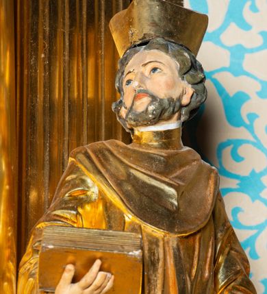 Zdjęcie nr 1: Rzeźba ścięta z tyłu, ustawiona na cokole. Święty ukazany frontalnie, w kontrapoście, z głową skierowaną w prawo. Lewą rękę ma opuszczonĄ w dół, prawą podtrzymuje zamkniętĄ księgę. Twarz ma kwadratową, o dużych, migdałowatych oczach, krótkim, prostym nosie i wąskich ustach, okolonĄ krótkimi, kręconymi włosami i brodą. Na głowie ma biret. Ubrany jest w togę profesorską o szerokich rękawach, z załogą (pelerynką). Polichromia ciała naturalistyczna, szaty i atrybuty złocone. 
