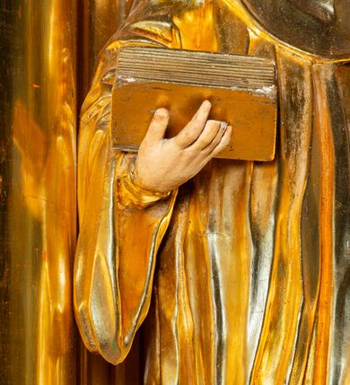 Zdjęcie nr 6: Rzeźba ścięta z tyłu, ustawiona na cokole. Święty ukazany frontalnie, w kontrapoście, z głową skierowaną w prawo. Lewą rękę ma opuszczonĄ w dół, prawą podtrzymuje zamkniętĄ księgę. Twarz ma kwadratową, o dużych, migdałowatych oczach, krótkim, prostym nosie i wąskich ustach, okolonĄ krótkimi, kręconymi włosami i brodą. Na głowie ma biret. Ubrany jest w togę profesorską o szerokich rękawach, z załogą (pelerynką). Polichromia ciała naturalistyczna, szaty i atrybuty złocone. 
