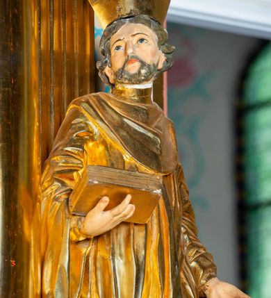 Zdjęcie nr 4: Rzeźba ścięta z tyłu, ustawiona na cokole. Święty ukazany frontalnie, w kontrapoście, z głową skierowaną w prawo. Lewą rękę ma opuszczonĄ w dół, prawą podtrzymuje zamkniętĄ księgę. Twarz ma kwadratową, o dużych, migdałowatych oczach, krótkim, prostym nosie i wąskich ustach, okolonĄ krótkimi, kręconymi włosami i brodą. Na głowie ma biret. Ubrany jest w togę profesorską o szerokich rękawach, z załogą (pelerynką). Polichromia ciała naturalistyczna, szaty i atrybuty złocone. 
