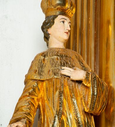 Zdjęcie nr 8: Rzeźba ścięta z tyłu, ustawiona na cokole. Święty ukazany frontalnie, w kontrapoście, z głową skierowaną w lewo. Prawą rękę ma opuszczoną, lewa spoczywa na piersi. Twarz ma kwadratową, o wyodrębnionej brodzie, młodzieńczych rysach, dużych, migdałowatych oczach, krótkim, prostym nosie i wąskich, rozchylonych ustach, okoloną krótkimi, kręconymi, brązowymi włosami. Na głowie ma mitrę książęcą. Ubrany jest w długą tunikę oraz rozchylony z przodu płaszcz królewski, o szerokich rękawach, z gronostajową pelerynką. Polichromia w partiach ciała naturalistyczna, szaty złocone. 

