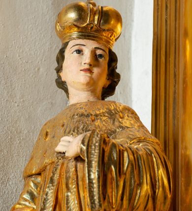 Zdjęcie nr 1: Rzeźba ścięta z tyłu, ustawiona na cokole. Święty ukazany frontalnie, w kontrapoście, z głową skierowaną w lewo. Prawą rękę ma opuszczoną, lewa spoczywa na piersi. Twarz ma kwadratową, o wyodrębnionej brodzie, młodzieńczych rysach, dużych, migdałowatych oczach, krótkim, prostym nosie i wąskich, rozchylonych ustach, okoloną krótkimi, kręconymi, brązowymi włosami. Na głowie ma mitrę książęcą. Ubrany jest w długą tunikę oraz rozchylony z przodu płaszcz królewski, o szerokich rękawach, z gronostajową pelerynką. Polichromia w partiach ciała naturalistyczna, szaty złocone. 

