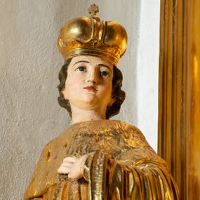 Zdjęcie nr 1: Rzeźba ścięta z tyłu, ustawiona na cokole. Święty ukazany frontalnie, w kontrapoście, z głową skierowaną w lewo. Prawą rękę ma opuszczoną, lewa spoczywa na piersi. Twarz ma kwadratową, o wyodrębnionej brodzie, młodzieńczych rysach, dużych, migdałowatych oczach, krótkim, prostym nosie i wąskich, rozchylonych ustach, okoloną krótkimi, kręconymi, brązowymi włosami. Na głowie ma mitrę książęcą. Ubrany jest w długą tunikę oraz rozchylony z przodu płaszcz królewski, o szerokich rękawach, z gronostajową pelerynką. Polichromia w partiach ciała naturalistyczna, szaty złocone. 

