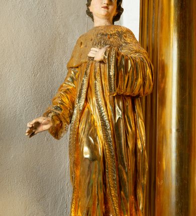 Zdjęcie nr 14: Rzeźba ścięta z tyłu, ustawiona na cokole. Święty ukazany frontalnie, w kontrapoście, z głową skierowaną w lewo. Prawą rękę ma opuszczoną, lewa spoczywa na piersi. Twarz ma kwadratową, o wyodrębnionej brodzie, młodzieńczych rysach, dużych, migdałowatych oczach, krótkim, prostym nosie i wąskich, rozchylonych ustach, okoloną krótkimi, kręconymi, brązowymi włosami. Na głowie ma mitrę książęcą. Ubrany jest w długą tunikę oraz rozchylony z przodu płaszcz królewski, o szerokich rękawach, z gronostajową pelerynką. Polichromia w partiach ciała naturalistyczna, szaty złocone. 

