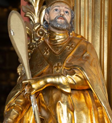 Zdjęcie nr 1: Rzeźba ścięta z tyłu, ustawiona na cokole. Święty ukazany frontalnie, w kontrapoście, z głową skierowaną w lewo. W prawej ręce trzyma laskę zakończoną potrójnym krzyżem (papieskim), w lewej krótkie wiosło. Twarz ma kwadratową, o dużych, migdałowatych oczach, krótkim, prostym nosie i małych, rozchylonych ustach, okoloną siwymi, kręconymi, krótkimi włosami i brodą. Na głowie ma infułę. Ubrany jest w albę, rokietę z dekoracyjną lamówką, kapę o rytym wzorze, na piersi ma paliusz. Polichromia ciała naturalistyczna, szaty i atrybuty złocone. 
