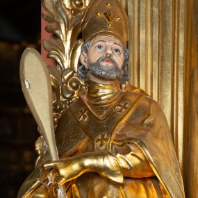 Zdjęcie nr 1: Rzeźba ścięta z tyłu, ustawiona na cokole. Święty ukazany frontalnie, w kontrapoście, z głową skierowaną w lewo. W prawej ręce trzyma laskę zakończoną potrójnym krzyżem (papieskim), w lewej krótkie wiosło. Twarz ma kwadratową, o dużych, migdałowatych oczach, krótkim, prostym nosie i małych, rozchylonych ustach, okoloną siwymi, kręconymi, krótkimi włosami i brodą. Na głowie ma infułę. Ubrany jest w albę, rokietę z dekoracyjną lamówką, kapę o rytym wzorze, na piersi ma paliusz. Polichromia ciała naturalistyczna, szaty i atrybuty złocone. 
