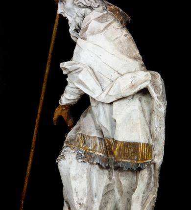 Zdjęcie nr 2: Rzeźba w całej postaci ukazuje frontalnie św. Augustyna ujętego w mocnym kontrapoście. Święty podniesioną prawą ręką trzyma pastorał, lewą zaś zdaje się odbierać rybę podawana mu przez nagie putto widniejące u jego stóp. Biskup w wysokiej infule ma pociągłą twarz o zapadniętych policzkach otoczoną rozwianą, długa brodą oraz kędzierzawymi włosami wystającymi spod złoconej infuły. Jego twarz charakteryzuje wydatny nos i usta. Ubrany jest w rozwianą mocno drapowaną sutannę, komżę obszytą u spodu frędzlą oraz kapę spiętą pod szyją. Spod sutanny widoczny jest stopa obuta w trzewik. Nagie putto u stóp biskua zostało ukazane w kontrapoście w trzech czwartych w prawo. Obiema rękami podaje świętemu rybę. Fragment jego biodra zasłani rozwiana tkanina. Putto wraz z biskupem stoją na fragmencie brzegu. 