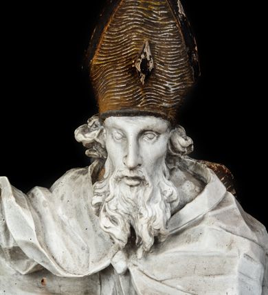 Zdjęcie nr 3: Rzeźba w całej postaci ukazuje frontalnie św. Augustyna ujętego w mocnym kontrapoście. Święty podniesioną prawą ręką trzyma pastorał, lewą zaś zdaje się odbierać rybę podawana mu przez nagie putto widniejące u jego stóp. Biskup w wysokiej infule ma pociągłą twarz o zapadniętych policzkach otoczoną rozwianą, długa brodą oraz kędzierzawymi włosami wystającymi spod złoconej infuły. Jego twarz charakteryzuje wydatny nos i usta. Ubrany jest w rozwianą mocno drapowaną sutannę, komżę obszytą u spodu frędzlą oraz kapę spiętą pod szyją. Spod sutanny widoczny jest stopa obuta w trzewik. Nagie putto u stóp biskua zostało ukazane w kontrapoście w trzech czwartych w prawo. Obiema rękami podaje świętemu rybę. Fragment jego biodra zasłani rozwiana tkanina. Putto wraz z biskupem stoją na fragmencie brzegu. 