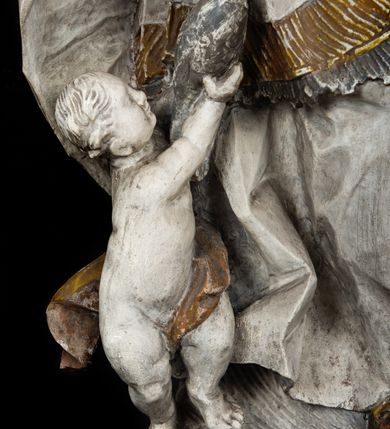 Zdjęcie nr 7: Rzeźba w całej postaci ukazuje frontalnie św. Augustyna ujętego w mocnym kontrapoście. Święty podniesioną prawą ręką trzyma pastorał, lewą zaś zdaje się odbierać rybę podawana mu przez nagie putto widniejące u jego stóp. Biskup w wysokiej infule ma pociągłą twarz o zapadniętych policzkach otoczoną rozwianą, długa brodą oraz kędzierzawymi włosami wystającymi spod złoconej infuły. Jego twarz charakteryzuje wydatny nos i usta. Ubrany jest w rozwianą mocno drapowaną sutannę, komżę obszytą u spodu frędzlą oraz kapę spiętą pod szyją. Spod sutanny widoczny jest stopa obuta w trzewik. Nagie putto u stóp biskua zostało ukazane w kontrapoście w trzech czwartych w prawo. Obiema rękami podaje świętemu rybę. Fragment jego biodra zasłani rozwiana tkanina. Putto wraz z biskupem stoją na fragmencie brzegu. 