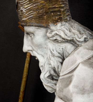 Zdjęcie nr 6: Rzeźba w całej postaci ukazuje frontalnie św. Augustyna ujętego w mocnym kontrapoście. Święty podniesioną prawą ręką trzyma pastorał, lewą zaś zdaje się odbierać rybę podawana mu przez nagie putto widniejące u jego stóp. Biskup w wysokiej infule ma pociągłą twarz o zapadniętych policzkach otoczoną rozwianą, długa brodą oraz kędzierzawymi włosami wystającymi spod złoconej infuły. Jego twarz charakteryzuje wydatny nos i usta. Ubrany jest w rozwianą mocno drapowaną sutannę, komżę obszytą u spodu frędzlą oraz kapę spiętą pod szyją. Spod sutanny widoczny jest stopa obuta w trzewik. Nagie putto u stóp biskua zostało ukazane w kontrapoście w trzech czwartych w prawo. Obiema rękami podaje świętemu rybę. Fragment jego biodra zasłani rozwiana tkanina. Putto wraz z biskupem stoją na fragmencie brzegu. 