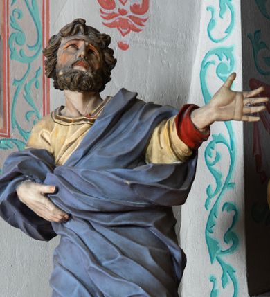Zdjęcie nr 1: Rzeźba ścięta z tyłu i drążona. Święty zwrócony w trzech czwartych w lewo, w kontrapoście, z uniesiona głową. Lewą, uniesioną rękę wyciąga w bok, prawą podtrzymuje z przodu połę płaszcza. Twarz ma szczupłą, kwadratową, o migdałowatych oczach skierowanych w górę, ostrym profilu nosa oraz wąskich rozchylonych ustach. Włosy i broda brązowe, krótkie, rzeźbione w silnie skręcone, pojedyncze pukle. Ubrany jest w jasnożółtą, silnie drapowaną tunikę ze złoconą lamówką oraz niebieski płaszcz zarzucony na ramiona i zawinięty wokół ciała postaci, silnie skręcony, drapowany i rozwiany od spodu, zdobiony brązową lamówką i podbity czerwonym podbiciem. Polichromia ciała naturalistyczna.