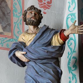 Zdjęcie nr 1: Rzeźba ścięta z tyłu i drążona. Święty zwrócony w trzech czwartych w lewo, w kontrapoście, z uniesiona głową. Lewą, uniesioną rękę wyciąga w bok, prawą podtrzymuje z przodu połę płaszcza. Twarz ma szczupłą, kwadratową, o migdałowatych oczach skierowanych w górę, ostrym profilu nosa oraz wąskich rozchylonych ustach. Włosy i broda brązowe, krótkie, rzeźbione w silnie skręcone, pojedyncze pukle. Ubrany jest w jasnożółtą, silnie drapowaną tunikę ze złoconą lamówką oraz niebieski płaszcz zarzucony na ramiona i zawinięty wokół ciała postaci, silnie skręcony, drapowany i rozwiany od spodu, zdobiony brązową lamówką i podbity czerwonym podbiciem. Polichromia ciała naturalistyczna.