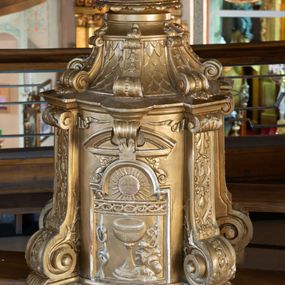 Zdjęcie nr 1: Tabernakulum w formie drewnianej, prostopadłościennej skrzynki, o wypukłym licu, na niskim, profilowanym cokole, ujętej w czterech narożach pilastrami o trzonach przechodzących w spływy wolutowe dekorowane kampanulami i ornamentem z tkaniny oraz muszlami. Pilastry dźwigają profilowany gzyms opasujący tabernakulum. Drzwiczki w formie stojącego prostokąta zamkniętego łukiem półkolistym nadwieszonym, w profilowanej ramie z płaskorzeźbionym przedstawieniem kielicha z unoszącą się nad nim hostią w glorii, z powrozem, motywem korony cierniowej oraz skałą z monogramem IHS. Nad drzwiczkami przyczółek, przerwany pośrodku konsolą podtrzymującą gzyms z wolutami i wstęgą w przyłuczach drzwiczek. Tron wystawienia w formie cokołu zwężającego się ku górze ujętego pięcioma spływami wolutowymi dekorowanymi kampanulami i perełkowaniem, pokryty rzeźbioną łuską; zwieńczony profilowaniem oraz szerszą podstawą dekorowaną ornamentem roślinnym. Struktura w całości złocona.