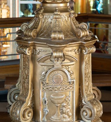 Zdjęcie nr 2: Tabernakulum w formie drewnianej, prostopadłościennej skrzynki, o wypukłym licu, na niskim, profilowanym cokole, ujętej w czterech narożach pilastrami o trzonach przechodzących w spływy wolutowe dekorowane kampanulami i ornamentem z tkaniny oraz muszlami. Pilastry dźwigają profilowany gzyms opasujący tabernakulum. Drzwiczki w formie stojącego prostokąta zamkniętego łukiem półkolistym nadwieszonym, w profilowanej ramie z płaskorzeźbionym przedstawieniem kielicha z unoszącą się nad nim hostią w glorii, z powrozem, motywem korony cierniowej oraz skałą z monogramem IHS. Nad drzwiczkami przyczółek, przerwany pośrodku konsolą podtrzymującą gzyms z wolutami i wstęgą w przyłuczach drzwiczek. Tron wystawienia w formie cokołu zwężającego się ku górze ujętego pięcioma spływami wolutowymi dekorowanymi kampanulami i perełkowaniem, pokryty rzeźbioną łuską; zwieńczony profilowaniem oraz szerszą podstawą dekorowaną ornamentem roślinnym. Struktura w całości złocona.