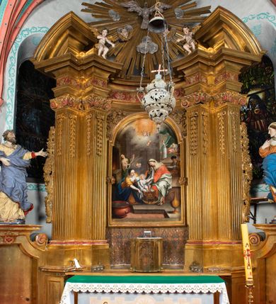 Zdjęcie nr 42: Nastawa architektoniczna, jednokondygnacyjna z glorią, jednoosiowa z bramkami, ustawiona na dwustrefowym cokole, na planie półowalu. Ołtarz kamienny, prostopadłościenny, z wcięciami na bocznych ściankach, zakończony profilowanym gzymsem; mensa kamienna. Na ściance frontowej namalowana scena Ostatniej Wieczerzy. Na ołtarzu ustawione drewniane tabernakulum obite blachą, w formie prostopadłościanu o wypukłych bokach, w narożach ujętego pilastrami o kanelowanych trzonach, dźwigającymi profilowany gzyms. Drzwiczki dwuskrzydłowe, w formie stojącego prostokąta zamkniętego łukiem półkolistym nadwieszonym, ujęty ramą z przedstawieniem baranka stojącego na ołtarzu, z którego piersi wypływa krew do kielicha; w górnej części monogram IHS. Nastawa ujęta dwiema parami filarów ustawionych pod kątem, o kanelowanych trzonach, dekorowanych kampanulami, podtrzymujących pełne belkowanie wyłamane na ich osi, z silnie wysuniętym gzymsem. Fryz zdobiony ornamentem roślinnym, w jego centrum kartusz z napisem „SANCTVS”. Na belkowaniu fragmenty zdwojonego, półkolistego przyczółka, z siedzącymi puttami. Pole główne wypełnione wnęką w formie stojącego prostokąta zamkniętego łukiem półkolistym nadwieszonym, ujęta profilowaną ramą, z obrazem Narodzenia Najświętszej Marii Panny. W przyłuczach dekoracja roślinna. Nastawa flankowana uszami utworzonymi z karbowanej wstęgi i ornamentu roślinnego. W miejscu zwieńczenia gołębica Ducha Świętego w otoku z obłoków i uskrzydlonych główek anielskich, w glorii promienistej. Bramki z drzwiczkami w formie stojącego prostokąta o wklęsłych górnych narożach ze ślimacznicami, ujęte grubą opaską, zwieńczone kluczem z herbem Uniwersytetu Jagiellońskiego oraz fragmentem profilowanego gzymsu, który stanowi podstawę dla figur św. Anny i św. Joachima. Herb lewej bramki z syglami „M[atthaeus] F[ranciscus]  K[alewski] / D[ecanus] S[antae] A[nnae] / C[uratus] Z[elenensis]”, herb prawej bramki z inskrypcją „A[NNO] D[OMINI] / 17/28”. Struktura w całości złocona, detale glorii srebrzone. Na odwrocie nastawy inskrypcja: „ODNOWIONO OŁTARZ ZA STARANIEM / KS(IĘDZA) JANA MICHALIKA. R(OKU) 1902.”