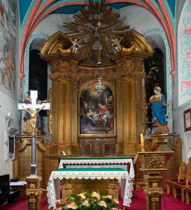 Zdjęcie nr 43: Nastawa architektoniczna, jednokondygnacyjna z glorią, jednoosiowa z bramkami, ustawiona na dwustrefowym cokole, na planie półowalu. Ołtarz kamienny, prostopadłościenny, z wcięciami na bocznych ściankach, zakończony profilowanym gzymsem; mensa kamienna. Na ściance frontowej namalowana scena Ostatniej Wieczerzy. Na ołtarzu ustawione drewniane tabernakulum obite blachą, w formie prostopadłościanu o wypukłych bokach, w narożach ujętego pilastrami o kanelowanych trzonach, dźwigającymi profilowany gzyms. Drzwiczki dwuskrzydłowe, w formie stojącego prostokąta zamkniętego łukiem półkolistym nadwieszonym, ujęty ramą z przedstawieniem baranka stojącego na ołtarzu, z którego piersi wypływa krew do kielicha; w górnej części monogram IHS. Nastawa ujęta dwiema parami filarów ustawionych pod kątem, o kanelowanych trzonach, dekorowanych kampanulami, podtrzymujących pełne belkowanie wyłamane na ich osi, z silnie wysuniętym gzymsem. Fryz zdobiony ornamentem roślinnym, w jego centrum kartusz z napisem „SANCTVS”. Na belkowaniu fragmenty zdwojonego, półkolistego przyczółka, z siedzącymi puttami. Pole główne wypełnione wnęką w formie stojącego prostokąta zamkniętego łukiem półkolistym nadwieszonym, ujęta profilowaną ramą, z obrazem Narodzenia Najświętszej Marii Panny. W przyłuczach dekoracja roślinna. Nastawa flankowana uszami utworzonymi z karbowanej wstęgi i ornamentu roślinnego. W miejscu zwieńczenia gołębica Ducha Świętego w otoku z obłoków i uskrzydlonych główek anielskich, w glorii promienistej. Bramki z drzwiczkami w formie stojącego prostokąta o wklęsłych górnych narożach ze ślimacznicami, ujęte grubą opaską, zwieńczone kluczem z herbem Uniwersytetu Jagiellońskiego oraz fragmentem profilowanego gzymsu, który stanowi podstawę dla figur św. Anny i św. Joachima. Herb lewej bramki z syglami „M[atthaeus] F[ranciscus]  K[alewski] / D[ecanus] S[antae] A[nnae] / C[uratus] Z[elenensis]”, herb prawej bramki z inskrypcją „A[NNO] D[OMINI] / 17/28”. Struktura w całości złocona, detale glorii srebrzone. Na odwrocie nastawy inskrypcja: „ODNOWIONO OŁTARZ ZA STARANIEM / KS(IĘDZA) JANA MICHALIKA. R(OKU) 1902.”