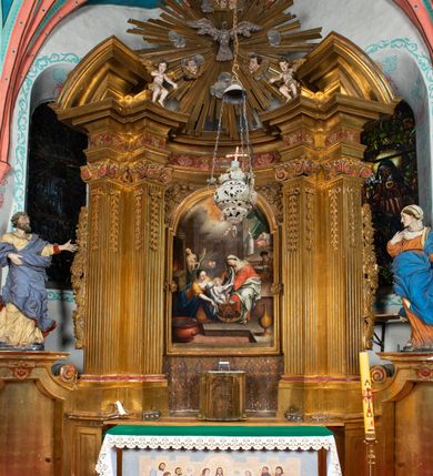 Zdjęcie nr 2: Nastawa architektoniczna, jednokondygnacyjna z glorią, jednoosiowa z bramkami, ustawiona na dwustrefowym cokole, na planie półowalu. Ołtarz kamienny, prostopadłościenny, z wcięciami na bocznych ściankach, zakończony profilowanym gzymsem; mensa kamienna. Na ściance frontowej namalowana scena Ostatniej Wieczerzy. Na ołtarzu ustawione drewniane tabernakulum obite blachą, w formie prostopadłościanu o wypukłych bokach, w narożach ujętego pilastrami o kanelowanych trzonach, dźwigającymi profilowany gzyms. Drzwiczki dwuskrzydłowe, w formie stojącego prostokąta zamkniętego łukiem półkolistym nadwieszonym, ujęty ramą z przedstawieniem baranka stojącego na ołtarzu, z którego piersi wypływa krew do kielicha; w górnej części monogram IHS. Nastawa ujęta dwiema parami filarów ustawionych pod kątem, o kanelowanych trzonach, dekorowanych kampanulami, podtrzymujących pełne belkowanie wyłamane na ich osi, z silnie wysuniętym gzymsem. Fryz zdobiony ornamentem roślinnym, w jego centrum kartusz z napisem „SANCTVS”. Na belkowaniu fragmenty zdwojonego, półkolistego przyczółka, z siedzącymi puttami. Pole główne wypełnione wnęką w formie stojącego prostokąta zamkniętego łukiem półkolistym nadwieszonym, ujęta profilowaną ramą, z obrazem Narodzenia Najświętszej Marii Panny. W przyłuczach dekoracja roślinna. Nastawa flankowana uszami utworzonymi z karbowanej wstęgi i ornamentu roślinnego. W miejscu zwieńczenia gołębica Ducha Świętego w otoku z obłoków i uskrzydlonych główek anielskich, w glorii promienistej. Bramki z drzwiczkami w formie stojącego prostokąta o wklęsłych górnych narożach ze ślimacznicami, ujęte grubą opaską, zwieńczone kluczem z herbem Uniwersytetu Jagiellońskiego oraz fragmentem profilowanego gzymsu, który stanowi podstawę dla figur św. Anny i św. Joachima. Herb lewej bramki z syglami „M[atthaeus] F[ranciscus]  K[alewski] / D[ecanus] S[antae] A[nnae] / C[uratus] Z[elenensis]”, herb prawej bramki z inskrypcją „A[NNO] D[OMINI] / 17/28”. Struktura w całości złocona, detale glorii srebrzone. Na odwrocie nastawy inskrypcja: „ODNOWIONO OŁTARZ ZA STARANIEM / KS(IĘDZA) JANA MICHALIKA. R(OKU) 1902.”