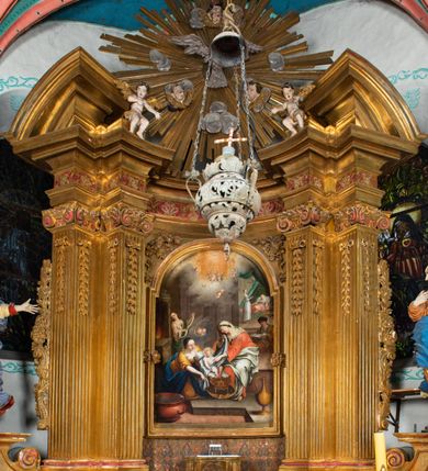 Zdjęcie nr 41: Nastawa architektoniczna, jednokondygnacyjna z glorią, jednoosiowa z bramkami, ustawiona na dwustrefowym cokole, na planie półowalu. Ołtarz kamienny, prostopadłościenny, z wcięciami na bocznych ściankach, zakończony profilowanym gzymsem; mensa kamienna. Na ściance frontowej namalowana scena Ostatniej Wieczerzy. Na ołtarzu ustawione drewniane tabernakulum obite blachą, w formie prostopadłościanu o wypukłych bokach, w narożach ujętego pilastrami o kanelowanych trzonach, dźwigającymi profilowany gzyms. Drzwiczki dwuskrzydłowe, w formie stojącego prostokąta zamkniętego łukiem półkolistym nadwieszonym, ujęty ramą z przedstawieniem baranka stojącego na ołtarzu, z którego piersi wypływa krew do kielicha; w górnej części monogram IHS. Nastawa ujęta dwiema parami filarów ustawionych pod kątem, o kanelowanych trzonach, dekorowanych kampanulami, podtrzymujących pełne belkowanie wyłamane na ich osi, z silnie wysuniętym gzymsem. Fryz zdobiony ornamentem roślinnym, w jego centrum kartusz z napisem „SANCTVS”. Na belkowaniu fragmenty zdwojonego, półkolistego przyczółka, z siedzącymi puttami. Pole główne wypełnione wnęką w formie stojącego prostokąta zamkniętego łukiem półkolistym nadwieszonym, ujęta profilowaną ramą, z obrazem Narodzenia Najświętszej Marii Panny. W przyłuczach dekoracja roślinna. Nastawa flankowana uszami utworzonymi z karbowanej wstęgi i ornamentu roślinnego. W miejscu zwieńczenia gołębica Ducha Świętego w otoku z obłoków i uskrzydlonych główek anielskich, w glorii promienistej. Bramki z drzwiczkami w formie stojącego prostokąta o wklęsłych górnych narożach ze ślimacznicami, ujęte grubą opaską, zwieńczone kluczem z herbem Uniwersytetu Jagiellońskiego oraz fragmentem profilowanego gzymsu, który stanowi podstawę dla figur św. Anny i św. Joachima. Herb lewej bramki z syglami „M[atthaeus] F[ranciscus]  K[alewski] / D[ecanus] S[antae] A[nnae] / C[uratus] Z[elenensis]”, herb prawej bramki z inskrypcją „A[NNO] D[OMINI] / 17/28”. Struktura w całości złocona, detale glorii srebrzone. Na odwrocie nastawy inskrypcja: „ODNOWIONO OŁTARZ ZA STARANIEM / KS(IĘDZA) JANA MICHALIKA. R(OKU) 1902.”