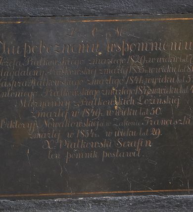 Zdjęcie nr 4: Rzeźba i nagrobek przyścienne. Nagrobek prostopadłościenny na cokole. Na nagrobku zamieszczona inskrypcja na marmurowej, wprawionej tablicy o wymiarach 70x 58 cm: „D.O.M./ Ku pobożnemu wspomnieniu/ Józefa Piątkowskiego zmarłego 1829 r: w wieku lat 70./ Magdaleny Piątkowskiej zmarłej 1855 r: w wieku lat 89./ Kaspra Piątkowskiego zmarłego 1847 r: w wieku lat 52./ Antoniego Piątkowskiego zmarłego 1847 r: w wieku lat 47./ Maryanny z Piątkowskich Łozińskiej/ zmarłej w 1849 r: w wieku lat 50./ Wiktoryj Nowakowskiej w Zakonie Franciszki zmarłej w 1854 r: w wieku lat 19/X: Piątkowski Serafin/ ten pomnik postawił”. Rzeźba ustawiona na nagrobku, przedstawia Michała Archanioła stojącego na smoku. Budowa ciała muskularna.Anioł w dynamicznej pozie, kontrapoście.Ciężar ciała oparty na prawej nodze. Tors i głowa silnie przechylone w lewą stronę. Ręce uniesione do wysokości ramion, ugięte w łokciach, przedramiona skierowane w dół. U ramion duże, dynamicznie ukształtowane skrzydła. Włosy kręcone, długością sięgające ramion, twarz o młodzieńczych rysach.W prawej dłoni trzyma miecz, skierowany ukośnie w dół, w stronę głowy smoka. Ubrany w zbroję łuskową, w dolnej partii zakończoną fartuchem złożonym zpasów, hełm z obfitym pióropuszem oraz sandały sięgające połowy łydki. Postać odziana jest w dekoracyjnie kształtowany płaszcz. Smok leżący na grzbiecie, pod stopami Archanioła, ma głowę i łapy wyciągnięte ku górze. Na grzbiecie łuska oraz skrzydła.