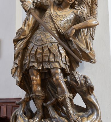 Zdjęcie nr 3: Rzeźba i nagrobek przyścienne. Nagrobek prostopadłościenny na cokole. Na nagrobku zamieszczona inskrypcja na marmurowej, wprawionej tablicy o wymiarach 70x 58 cm: „D.O.M./ Ku pobożnemu wspomnieniu/ Józefa Piątkowskiego zmarłego 1829 r: w wieku lat 70./ Magdaleny Piątkowskiej zmarłej 1855 r: w wieku lat 89./ Kaspra Piątkowskiego zmarłego 1847 r: w wieku lat 52./ Antoniego Piątkowskiego zmarłego 1847 r: w wieku lat 47./ Maryanny z Piątkowskich Łozińskiej/ zmarłej w 1849 r: w wieku lat 50./ Wiktoryj Nowakowskiej w Zakonie Franciszki zmarłej w 1854 r: w wieku lat 19/X: Piątkowski Serafin/ ten pomnik postawił”. Rzeźba ustawiona na nagrobku, przedstawia Michała Archanioła stojącego na smoku. Budowa ciała muskularna.Anioł w dynamicznej pozie, kontrapoście.Ciężar ciała oparty na prawej nodze. Tors i głowa silnie przechylone w lewą stronę. Ręce uniesione do wysokości ramion, ugięte w łokciach, przedramiona skierowane w dół. U ramion duże, dynamicznie ukształtowane skrzydła. Włosy kręcone, długością sięgające ramion, twarz o młodzieńczych rysach.W prawej dłoni trzyma miecz, skierowany ukośnie w dół, w stronę głowy smoka. Ubrany w zbroję łuskową, w dolnej partii zakończoną fartuchem złożonym zpasów, hełm z obfitym pióropuszem oraz sandały sięgające połowy łydki. Postać odziana jest w dekoracyjnie kształtowany płaszcz. Smok leżący na grzbiecie, pod stopami Archanioła, ma głowę i łapy wyciągnięte ku górze. Na grzbiecie łuska oraz skrzydła.