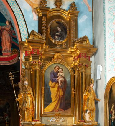 Zdjęcie nr 1: Nastawa architektoniczna, jednoosiowa, dwukondygnacyjna. Ołtarz prostopadłościenny, zwężający się ku dołowi, murowany, obłożony kamiennymi płytami, z krzyżem na froncie. 
Nastawa na niskim cokole, z wyodrębnionymi dwoma, ukośnie ustawionymi prostopadłościanami, z konsolami, dekorowanymi akantem i kampanulami. Pośrodku cokołu wyodrębniony postument dekorowany płyciną z akantem. Kondygnacja flankowana dwiema parami pilastrów o kanelowanych trzonach oraz ustawioną przed nimi parą kolumn o kapitelach kompozytowych. Podpory dźwigają pełne belkowanie, wyłamane na ich osi, z silnie wysuniętym gzymsem, z przerwanym architrawem i fryzem nad polem środkowym. Na belkowaniu fragmenty przerwanego, wolutowego przyczółka, zwrócone pod kątem, do wewnątrz. W polu środkowym wnęka w formie stojącego prostokąta zamkniętego łukiem półkolistym, ujęta profilowaną ramą dekorowaną na bokach kwiatami, zwieńczoną muszlą. We wnęce obraz św. Józefa z Dzieciątkiem. Poniżej wnęki płaskorzeźbione narzędzia stolarskie (piła, siekiera, kątownik, obcęgi) i stylizowany monogram świętego. Na konsolach, po bokach nastawy ustawione figury św. Wojciecha i św. Stanisława. Retabulum flankowane uszami utworzonymi z karbowanej wstęgi i ornamentu roślinnego. Druga kondygnacja węższa, ujęta ustawionymi pod kątem pilastrami, o trzonach dekorowanych kampanulami. Pilastry podtrzymują gzyms wyłamany na ich osi, nad polem przyjmujący kształt łuku półkolistego nadwieszonego. Na nim ustawione trzy wazony z kwiatami. W polu obraz św. Jana Kantego w formie stojącego owalu, ujęty ramą, dekorowaną ornamentem roślinnym. Struktura niemal w całości złocona, elementy cokołu i fryzu polichromowane w kolorze czerwonym, ornamentyka złocona. 
