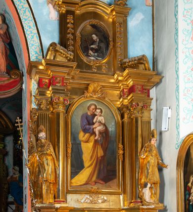 Zdjęcie nr 2: Nastawa architektoniczna, jednoosiowa, dwukondygnacyjna. Ołtarz prostopadłościenny, zwężający się ku dołowi, murowany, obłożony kamiennymi płytami, z krzyżem na froncie. 
Nastawa na niskim cokole, z wyodrębnionymi dwoma, ukośnie ustawionymi prostopadłościanami, z konsolami, dekorowanymi akantem i kampanulami. Pośrodku cokołu wyodrębniony postument dekorowany płyciną z akantem. Kondygnacja flankowana dwiema parami pilastrów o kanelowanych trzonach oraz ustawioną przed nimi parą kolumn o kapitelach kompozytowych. Podpory dźwigają pełne belkowanie, wyłamane na ich osi, z silnie wysuniętym gzymsem, z przerwanym architrawem i fryzem nad polem środkowym. Na belkowaniu fragmenty przerwanego, wolutowego przyczółka, zwrócone pod kątem, do wewnątrz. W polu środkowym wnęka w formie stojącego prostokąta zamkniętego łukiem półkolistym, ujęta profilowaną ramą dekorowaną na bokach kwiatami, zwieńczoną muszlą. We wnęce obraz św. Józefa z Dzieciątkiem. Poniżej wnęki płaskorzeźbione narzędzia stolarskie (piła, siekiera, kątownik, obcęgi) i stylizowany monogram świętego. Na konsolach, po bokach nastawy ustawione figury św. Wojciecha i św. Stanisława. Retabulum flankowane uszami utworzonymi z karbowanej wstęgi i ornamentu roślinnego. Druga kondygnacja węższa, ujęta ustawionymi pod kątem pilastrami, o trzonach dekorowanych kampanulami. Pilastry podtrzymują gzyms wyłamany na ich osi, nad polem przyjmujący kształt łuku półkolistego nadwieszonego. Na nim ustawione trzy wazony z kwiatami. W polu obraz św. Jana Kantego w formie stojącego owalu, ujęty ramą, dekorowaną ornamentem roślinnym. Struktura niemal w całości złocona, elementy cokołu i fryzu polichromowane w kolorze czerwonym, ornamentyka złocona. 
