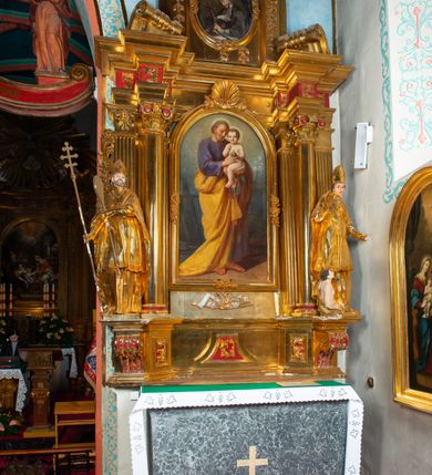 Zdjęcie nr 13: Nastawa architektoniczna, jednoosiowa, dwukondygnacyjna. Ołtarz prostopadłościenny, zwężający się ku dołowi, murowany, obłożony kamiennymi płytami, z krzyżem na froncie. 
Nastawa na niskim cokole, z wyodrębnionymi dwoma, ukośnie ustawionymi prostopadłościanami, z konsolami, dekorowanymi akantem i kampanulami. Pośrodku cokołu wyodrębniony postument dekorowany płyciną z akantem. Kondygnacja flankowana dwiema parami pilastrów o kanelowanych trzonach oraz ustawioną przed nimi parą kolumn o kapitelach kompozytowych. Podpory dźwigają pełne belkowanie, wyłamane na ich osi, z silnie wysuniętym gzymsem, z przerwanym architrawem i fryzem nad polem środkowym. Na belkowaniu fragmenty przerwanego, wolutowego przyczółka, zwrócone pod kątem, do wewnątrz. W polu środkowym wnęka w formie stojącego prostokąta zamkniętego łukiem półkolistym, ujęta profilowaną ramą dekorowaną na bokach kwiatami, zwieńczoną muszlą. We wnęce obraz św. Józefa z Dzieciątkiem. Poniżej wnęki płaskorzeźbione narzędzia stolarskie (piła, siekiera, kątownik, obcęgi) i stylizowany monogram świętego. Na konsolach, po bokach nastawy ustawione figury św. Wojciecha i św. Stanisława. Retabulum flankowane uszami utworzonymi z karbowanej wstęgi i ornamentu roślinnego. Druga kondygnacja węższa, ujęta ustawionymi pod kątem pilastrami, o trzonach dekorowanych kampanulami. Pilastry podtrzymują gzyms wyłamany na ich osi, nad polem przyjmujący kształt łuku półkolistego nadwieszonego. Na nim ustawione trzy wazony z kwiatami. W polu obraz św. Jana Kantego w formie stojącego owalu, ujęty ramą, dekorowaną ornamentem roślinnym. Struktura niemal w całości złocona, elementy cokołu i fryzu polichromowane w kolorze czerwonym, ornamentyka złocona. 
