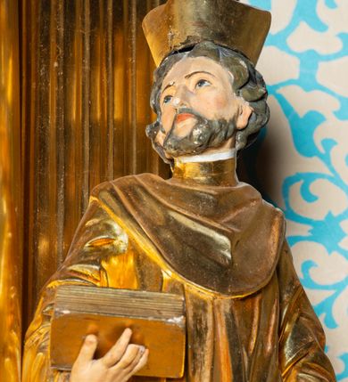 Zdjęcie nr 3: Nastawa architektoniczna, jednoosiowa, dwukondygnacyjna. Ołtarz murowany, prostopadłościenny, obity metalową blachą, zdobioną trybowaną kratownicą i gwiazdkami. Wewnątrz grób Chrystusa ze współczesną rzeźbą. Nastawa na niskim cokole, z wyodrębnionymi dwoma, ukośnie ustawionymi prostopadłościanami, z konsolami, dekorowanymi akantem i kampanulami. Pośrodku cokołu zamontowany obraz św. Faustyny w kształcie wieloboku. Kondygnacja flankowana dwiema parami pilastrów o kanelowanych trzonach oraz ustawioną przed nimi parą kolumn o kapitelach kompozytowych. Podpory dźwigają pełne belkowanie, wyłamane na ich osi, z silnie wysuniętym gzymsem, z przerwanym architrawem i fryzem nad polem środkowym. Na belkowaniu fragmenty przerwanego, wolutowego przyczółka, zwrócone pod kątem, do wewnątrz. W polu środkowym wnęka w formie stojącego prostokąta zamkniętego łukiem półkolistym, ujęta profilowaną ramą dekorowaną na bokach kwiatami, zwieńczoną muszlą. We wnęce obraz „Jezu Ufam Tobie”. Na konsolach, po bokach nastawy ustawione figury św. Kazimierza i św. Jana Kantego. Nastawa flankowana uszami utworzonymi z karbowanej wstęgi i ornamentu roślinnego. Druga kondygnacja węższa, flankowana ustawionymi pod kątem pilastrami, o trzonach dekorowanych kampanulami. Pilastry podtrzymują gzyms wyłamany na ich osi, nad polem przyjmujący kształt łuku półkolistego nadwieszonego. Na nim ustawione dwa wazony z kwiatami i bukiet kwiatów. W polu obraz św. Joachima w formie stojącego owalu, ujęty ramą, dekorowaną ornamentem roślinnym. Struktura niemal w całości złocona, elementy cokołu i fryzu polichromowane w kolorze czerwonym, ornamentyka złocona. 


